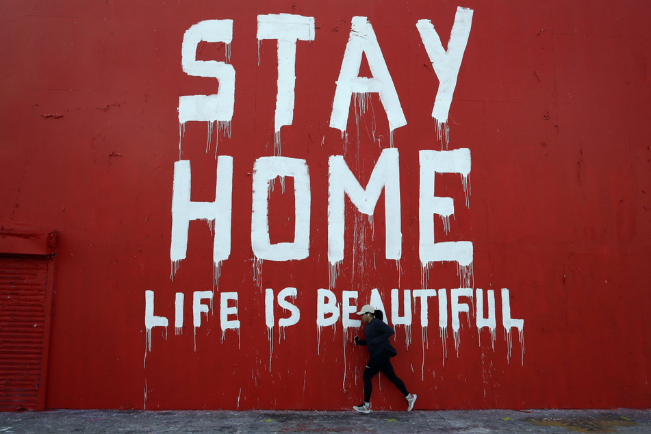 Ein Jogger läuft an einem Wandbild mit der Aufschrift "Stay Home - Life is beautiful" ("Bleib zu Hause, das Leben ist schön") vorbei.