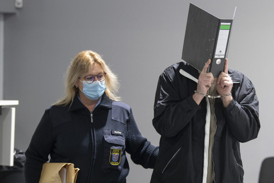 Mit Handschellen wird der Angeklagte in einen provisorischen Verhandlungssaal vom Landgericht Wiesbaden geführt (Archivfoto).