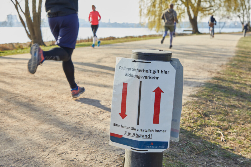 Jogger laufen an der Außenalster an einem Hinweisschild des Bezirksamtes Eimsbüttel vorbei.