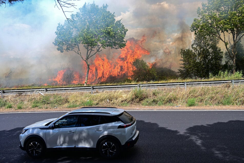 Ein Auto fährt an einem brennenden Waldstück bei Villeneuve-les-Beziers entlang.