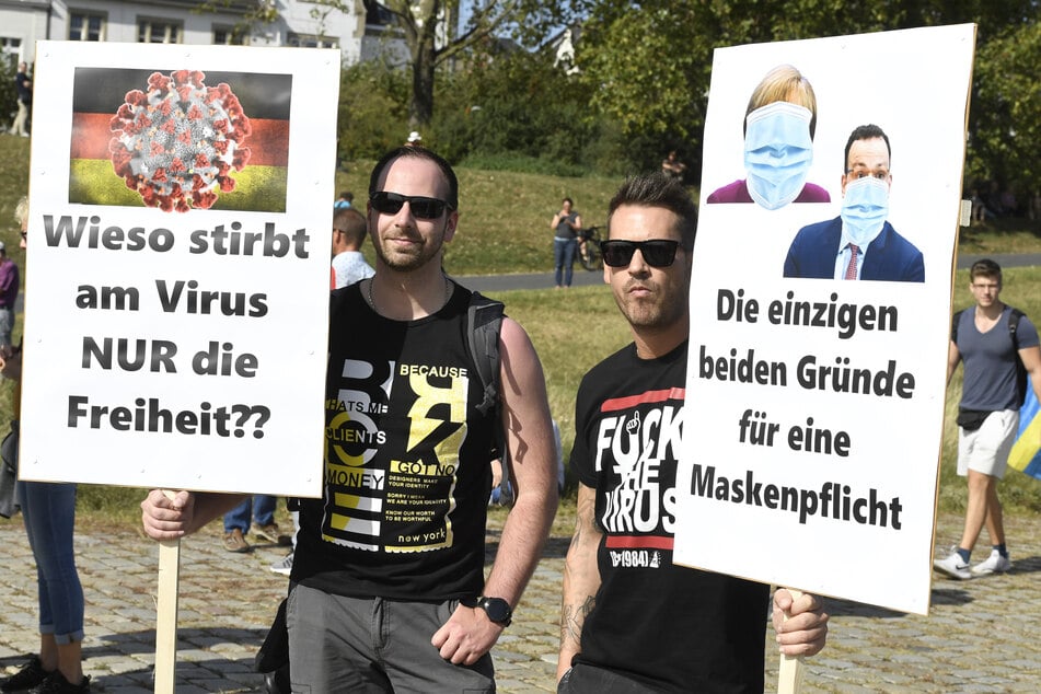 Zwei Männer halten Schilder auf den Düsseldorfer Rheinwiesen, vor einer Demonstration gegen die Maßnahmen zur Bekämpfung der Ausbreitung des Coronavirus.