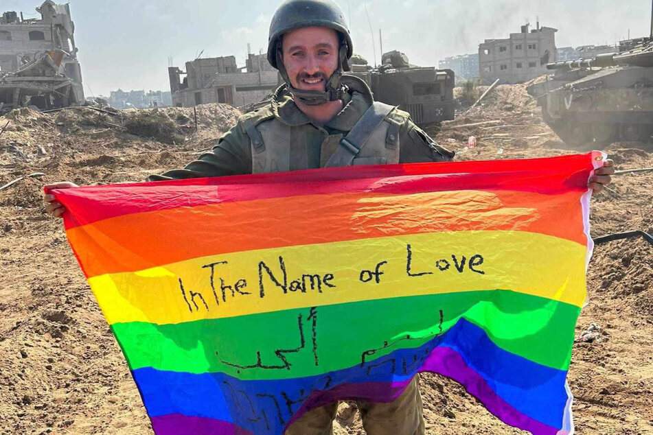 Israeli soldier Yoav Atzmoni holds up a gay pride flag reading "In The Name of Love" as he stands before the ruins of bombed Gaza.