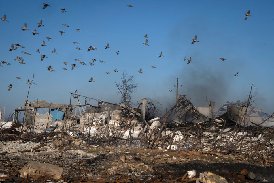 Vögel fliegen über den Rauch, der aus den Ruinen eines Bauernhofs und eines noch brennenden Getreidespeichers in der Ukraine aufsteigt.