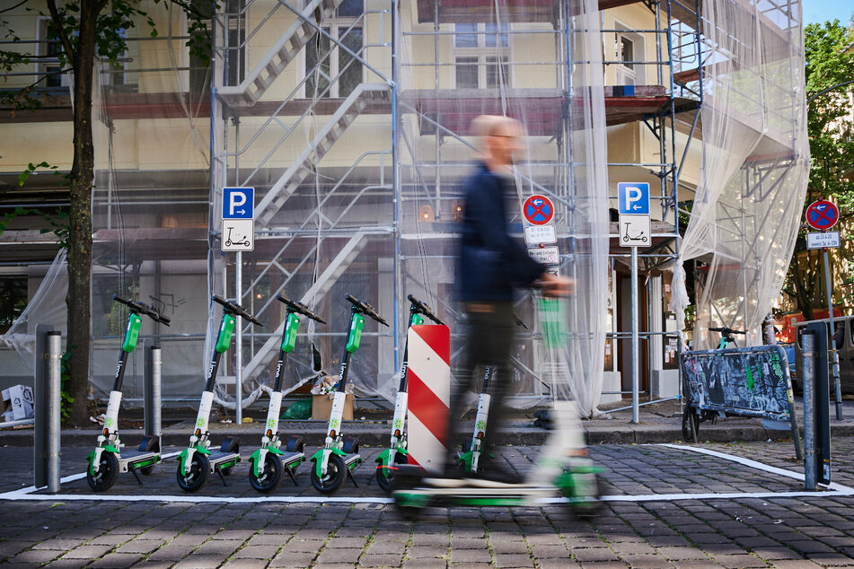 Ein Mann auf einem E-Scooter fährt an einem E-Scooter-Stellplatz in Berlin vorbei.