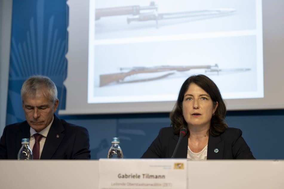 Polizeivizepräsident Guido Limmer (l.) und die Oberstaatsanwältin Gabriele Tilmann sitzen vor einem Foto der Tatwaffe in München.