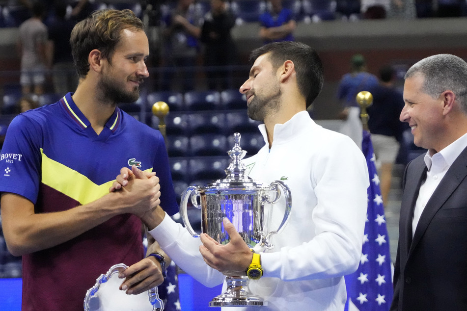 Novak Djokovic (c.) shakes hands with Daniil Medvedev (l.) during the trophy ceremony after their match in the men's singles final at the 2023 US Open.