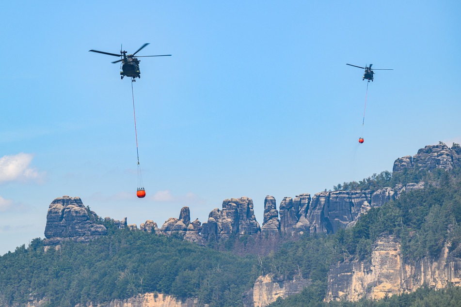 Hubschrauber der Bundeswehr fliegen mit Löschwasser-Außenlastbehältern, um die Brände zu bekämpfen.