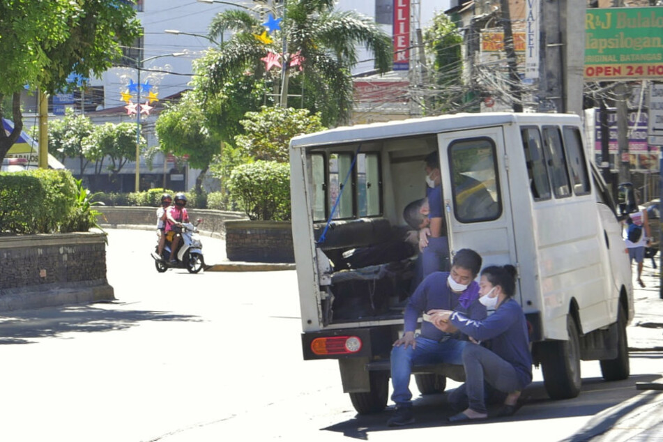 Philippinen, Mandaluyong City: Mitarbeiter des Gesundheitswesens ruhen sich an einem Kleintransporter aus.