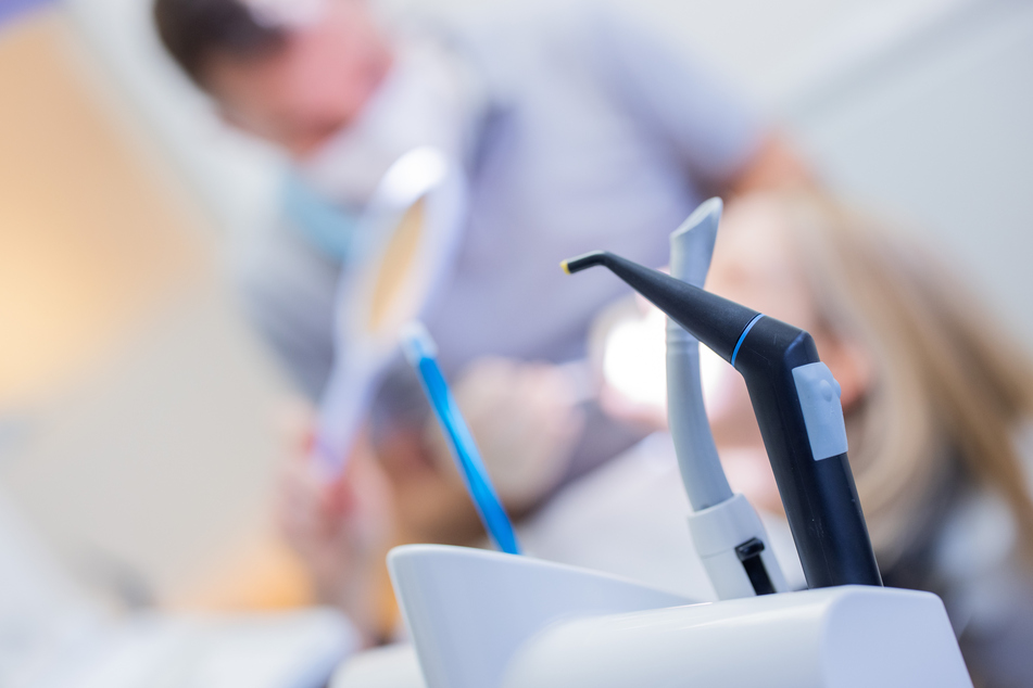 Ein Zahnarzt mit Mund-Nasen-Schutz und Schutzvisier versorgt eine Patientin in einer Praxis.