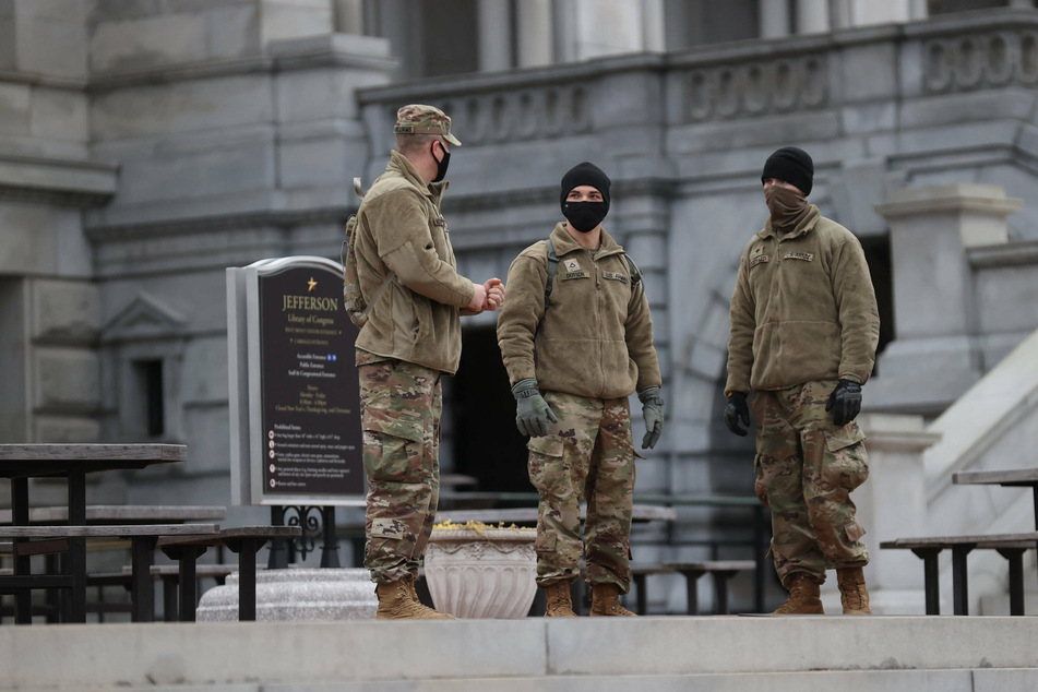 Police and National Guard stand watch over the Capitol building which now stands complete with non-scalable fencing and concrete barriers.