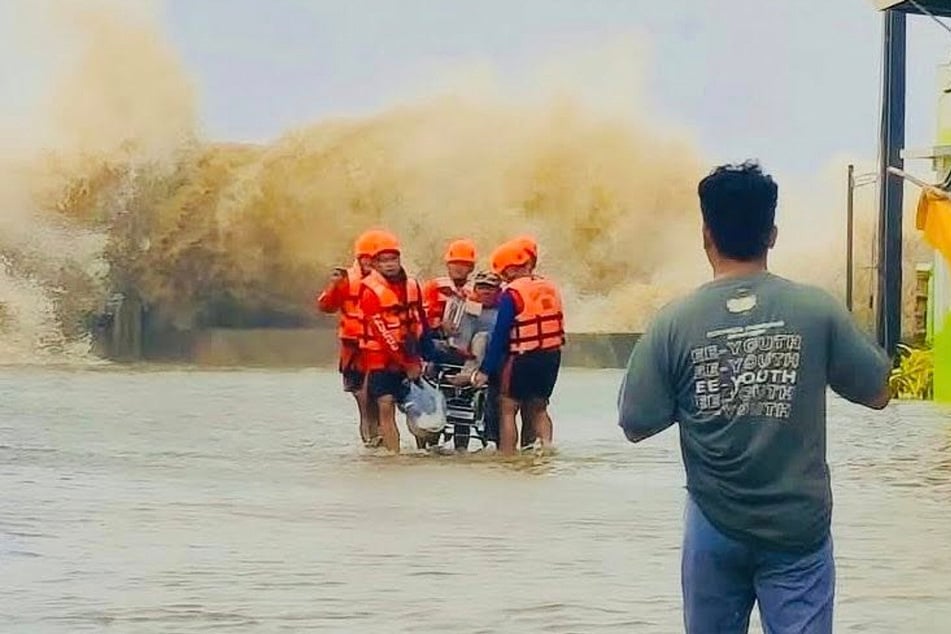 Philippinische Rettungskräfte evakuieren einen Bewohner in einem Rollstuhl, während die Wellen aufgrund des Tropensturms "Bualoi" brechen.