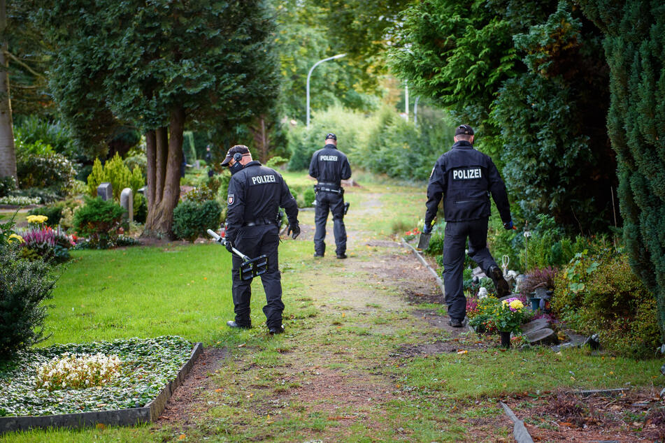 Mit einem Metalldetektor sucht die Polizei den Rendsburger Friedhof ab.
