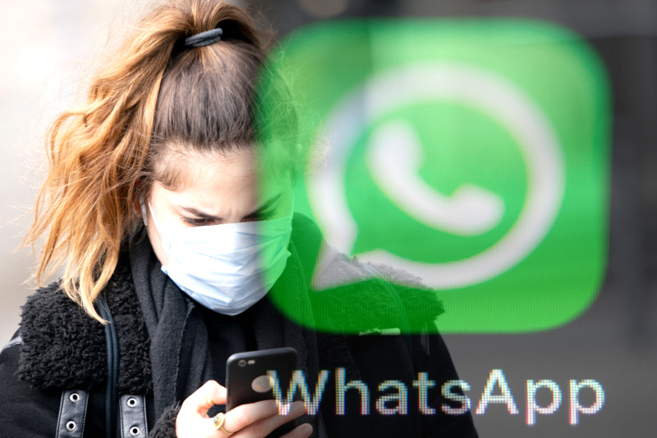 Mit einem Mundschutz im Gesicht tippt eine Frau auf ihrem Smartphone (Symbolbild).