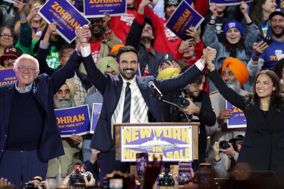 New York City mayoral candidate Zohran Mamdani (c.) holds hands with Senator Bernie Sanders (l.) and Representative Alexandria Ocasio-Cortez at the end of a campaign rally at Forest Hills Stadium in Queens on October 26, 2025.
