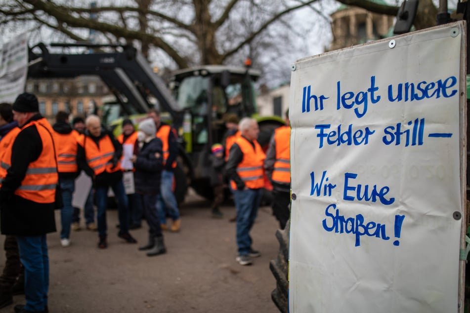 Bei einer Mahnwache vom Landesbauernverband Baden-Württemberg hängt ein Schild mit der Aufschrift "Ihr legt unsere Felder still - Wir eure Straßen" an einem Traktor.