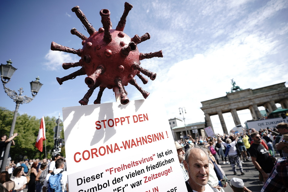 "Stoppt den Corona-Wahnsinn!" steht auf dem Schild eines Teilnehmers einer Demonstration gegen die Corona-Maßnahmen und dem Modell eines Coronavirus.