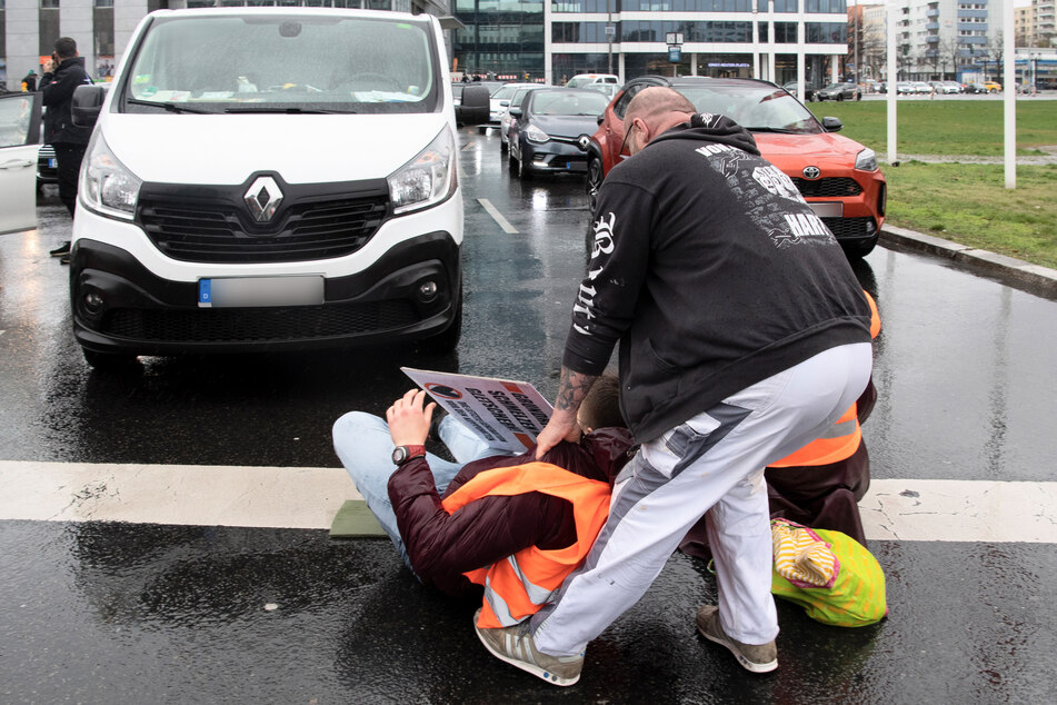 Ein genervter Autofahrer versucht einen Klimaaktivisten von der Straße zu entfernen.