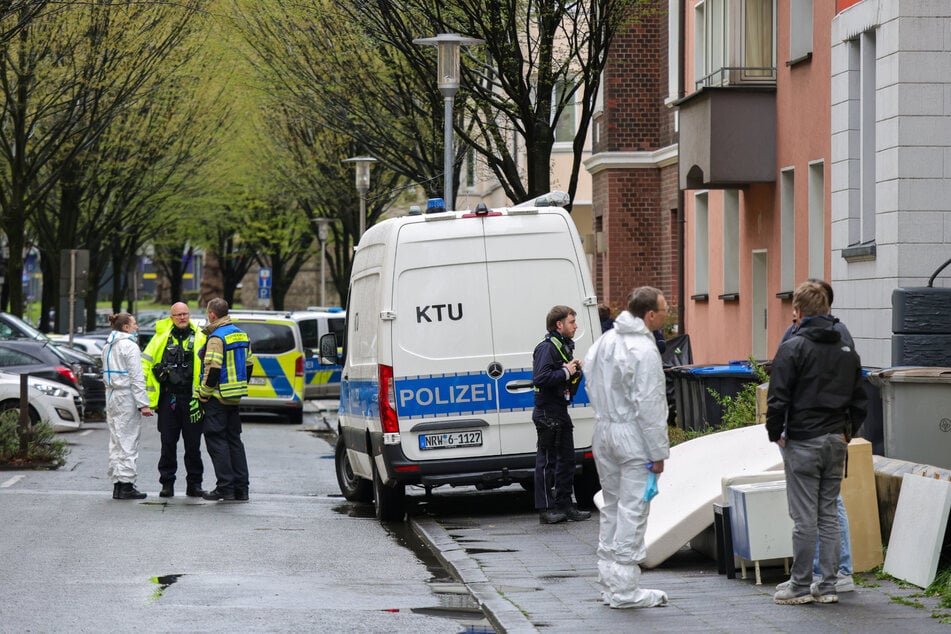 Vor dem Mehrfamilienhaus der Familie stehen Beamte der Polizei auf dem Gehweg und der Straße.