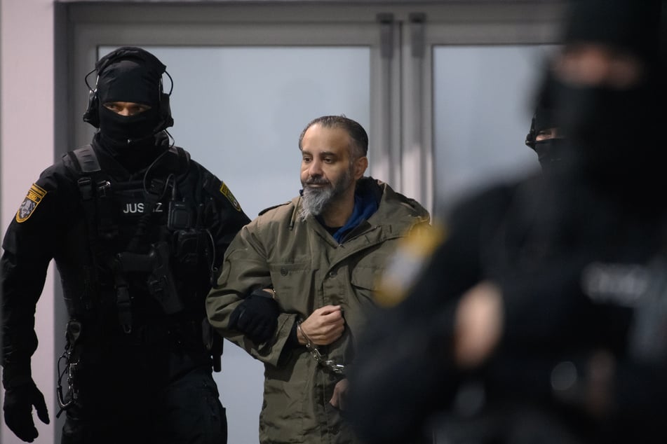 Der Angeklagte wird von bewaffneten Polizisten in seine Sicherheitskammer geführt.