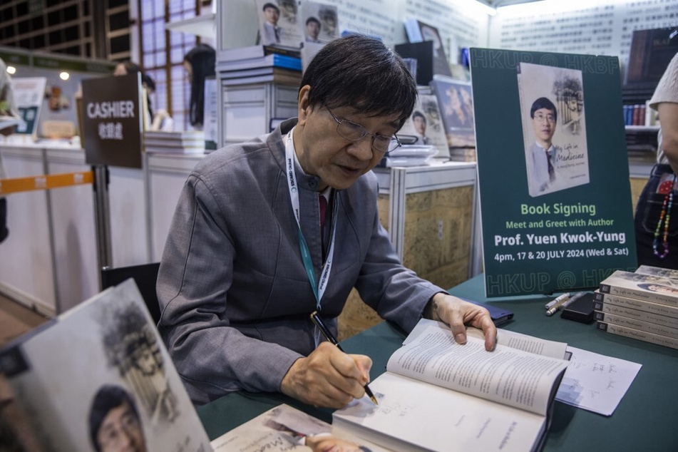 Microbiologist Yuen Kwok-yung signs copies of his new book during the annual book fair at the Hong Kong Convention and Exhibition Centre.