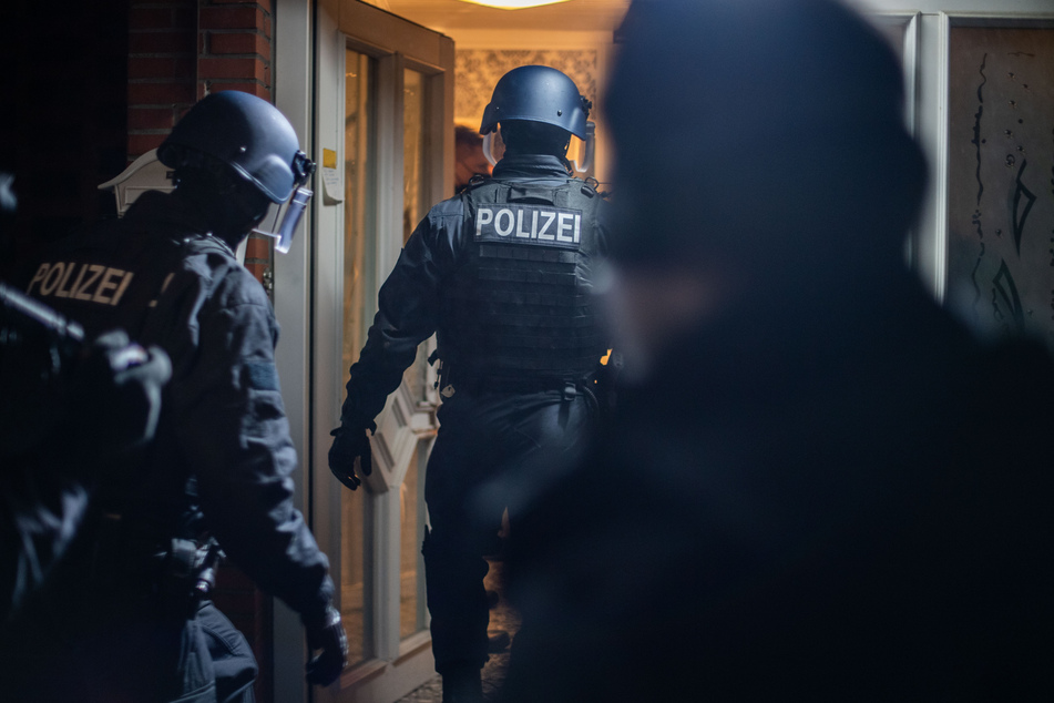 Einsatzkräfte der Polizei stürmen ein Haus, um es nach Verdächtigen zu durchsuchen.