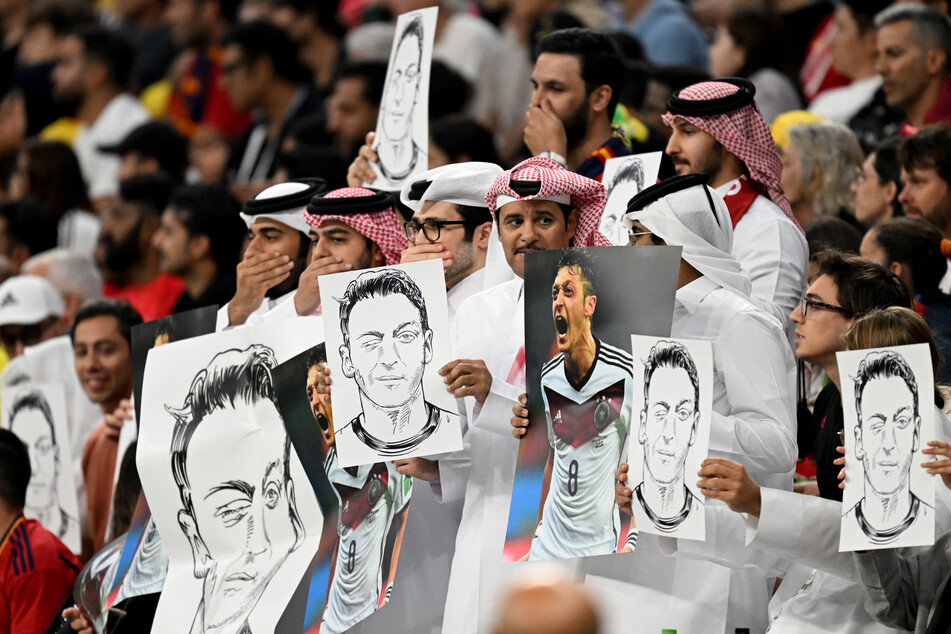 Zuschauer hatten während der Partie zwischen Spanien und Deutschland Plakate mit Fotos und Zeichnungen von Ex-DFB-Kicker Mesut Özil (34) hoch gehalten und sich zudem teils die Hand vor den Mund gehalten. Was es genau damit auf sich hatte, blieb bislang unbekannt.