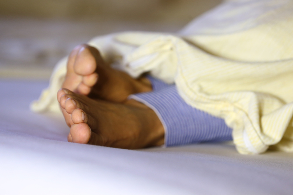 Die Füße einer Frau ragen am unter einer Bettdecke hervor.