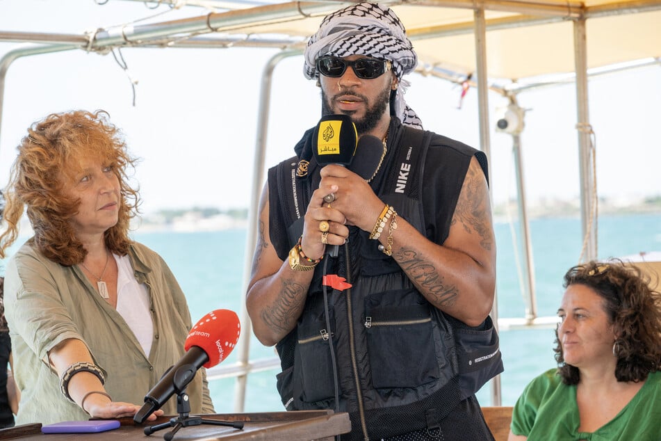 Chris Smalls (c.) addresses a press conference on the Freedom Flotilla ship Handala ahead of the boat's departure for Gaza at a port in Syracuse, Sicily, southern Italy, on July 13, 2025.