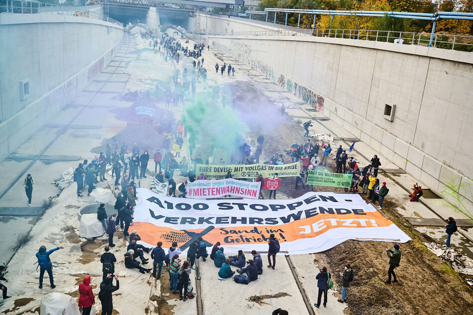Klimaaktivisten unterschiedlicher Bündnisse (Ende Gelände, Extinction Rebellion und Sand im Getriebe) halten ein Transparent mit der Aufschrift "A100 stoppen - Verkehrswende jetzt!" auf der Baustelle der A100.