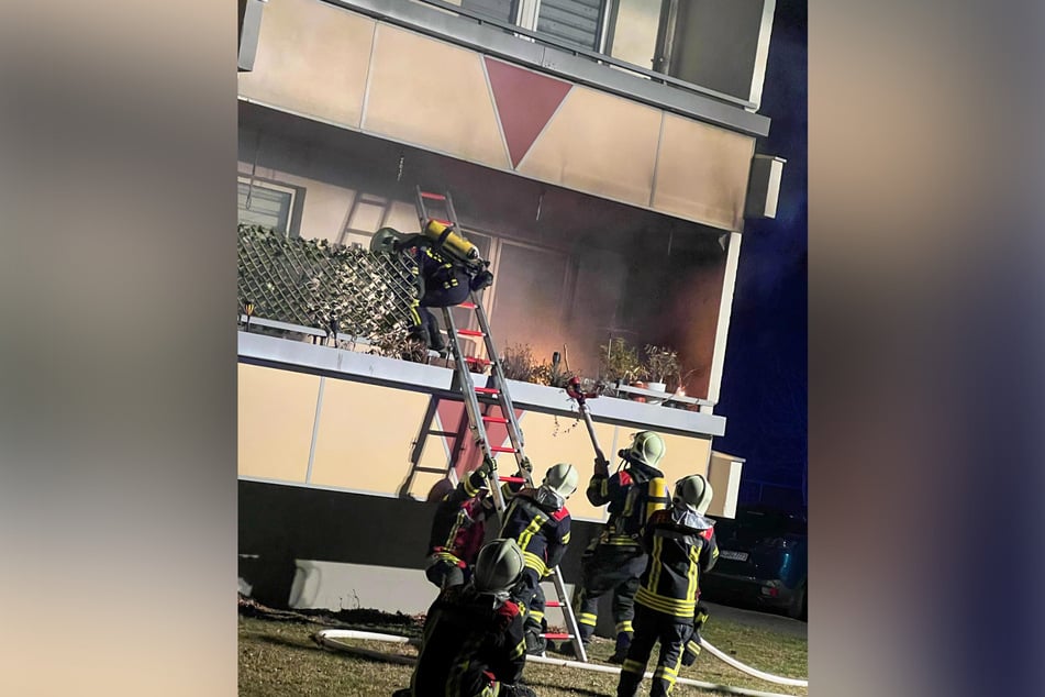 Feuerwehrleute bekämpfen Flammen auf einem Balkon im ersten Stockwerk eines Wohnblocks.