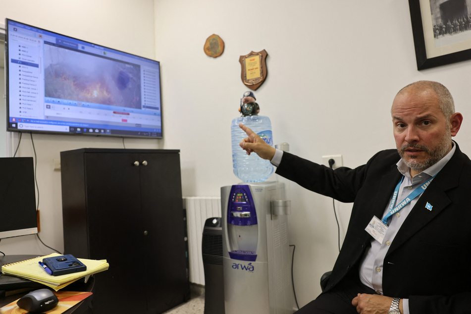 United Nations Relief and Works Agency for Palestine Refugees (UNRWA) Affairs Director in the West Bank Adam Bouloukos shows on a screen a video of a fire at the agency's headquarters in east Jerusalem, after "Israeli extremists" reportedly set ablaze the perimeter of the building on Friday.