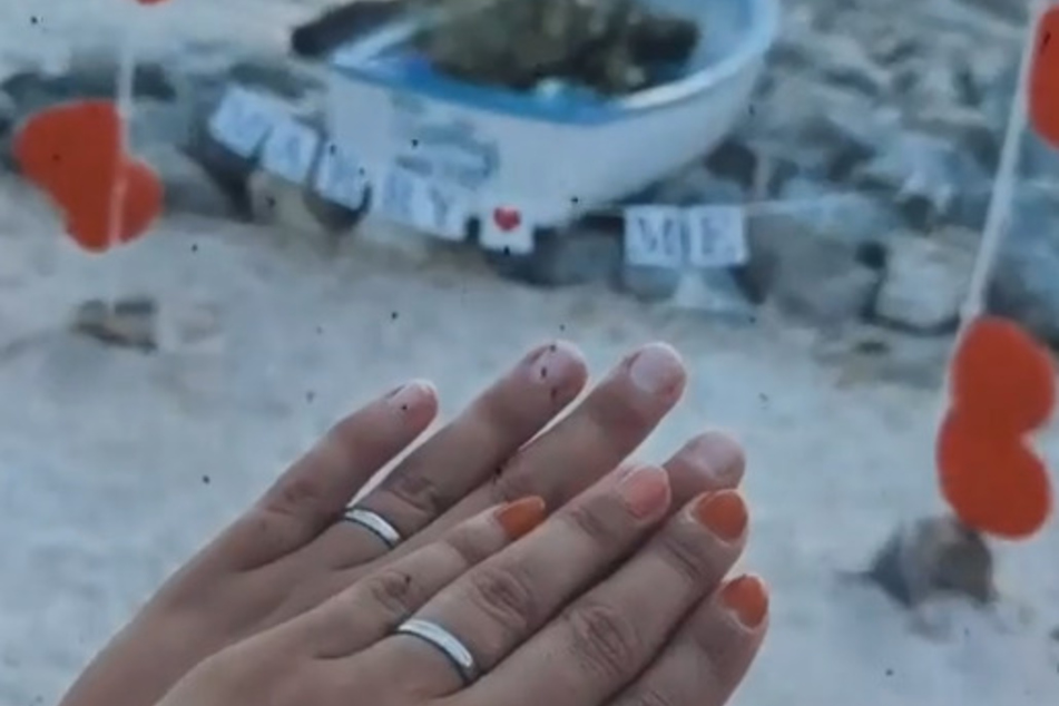 Stolz halten die beiden Turteltäubchen ihre Ringe in die Kamera und feiern den nächsten Schritt in ihrer Beziehung.