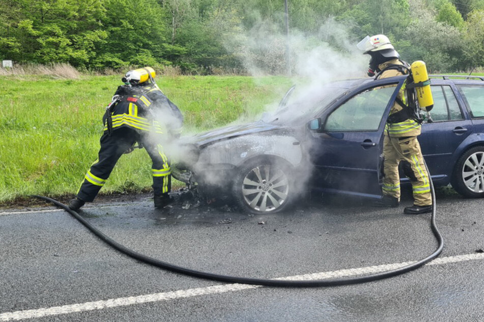 Zwei Kameraden der Feuerwehr stehen mit Atemschutzmasken an dem qualmenden VW-Golf.