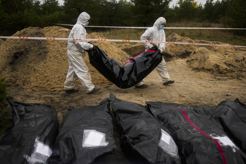 Kriegsverbrechern auf der Spur: Mitglieder eines forensischen Teams tragen einen Plastiksack mit einer Leiche, während sie an einer Exhumierung in einem Massengrab in Lyman arbeiten.