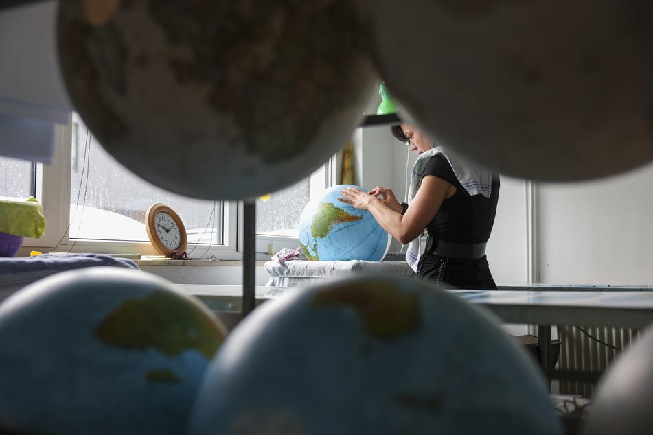 Eine Kaschiererin beklebt in Handarbeit einen Globus in der Firma Räthgloben. Dafür müssen die elliptischen Zuschnitte passgenau auf eine Kunststoff- oder Glaskugel geklebt werden.