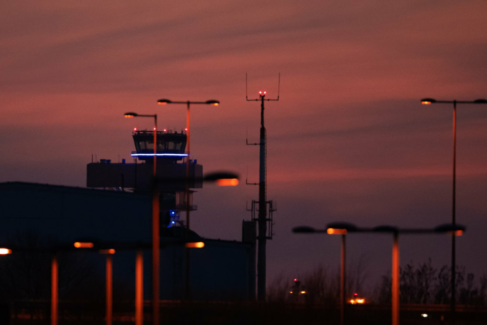 Lichtmasten und der Tower des künftigen Hauptstadtflughafens BER vor rotem Abendhimmel.