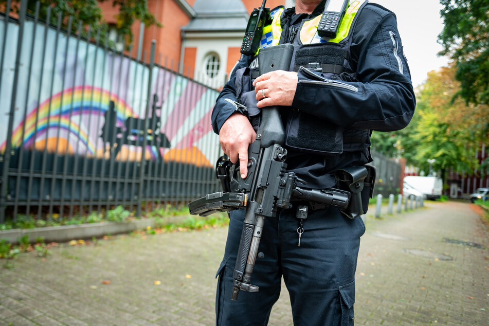 Ein Polizist mit Maschinenpistole steht auf dem Fußweg vor dem Zaun der jüdischen Talmud-Thora-Schule.