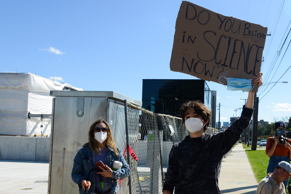 USA, Bethesda: Ein junger Mann hält ein Schild "Do you believe in Science now" (Glaubst du jetzt an die Wissenschaft) vor dem Militärkrankenhaus Walter Reed in Bethesda, in dem US-Präsident Trump nach einer Corona-Infektion behandelt wird.