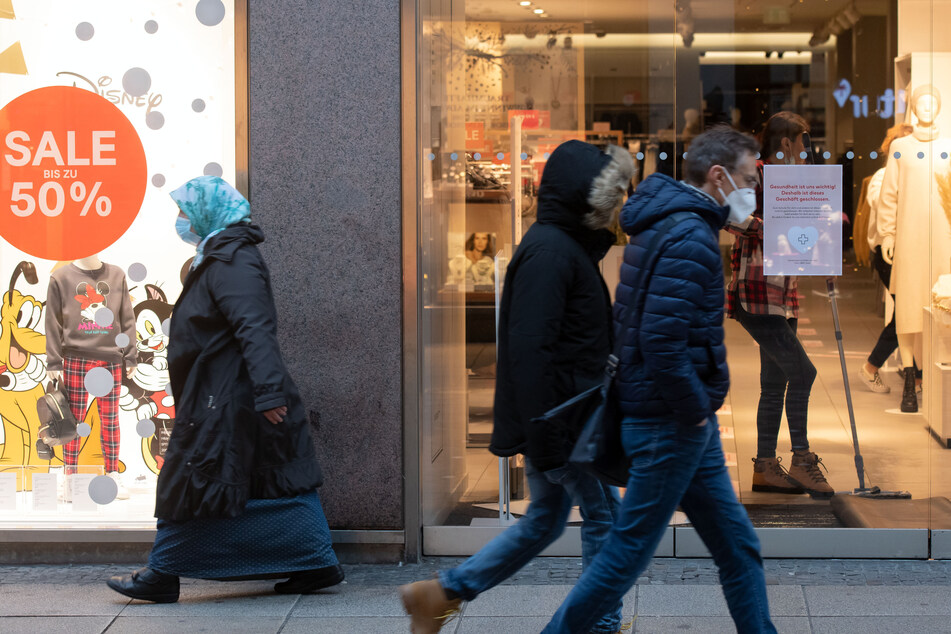 Passanten gehen an einem geschlossen Bekleidungsgeschäft vorbei.