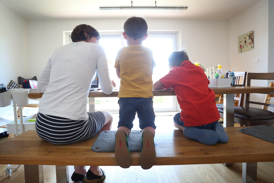 Die Mutter des sechsjährigen Jakob und des vierjährigen Valentin sitzt Zuhause neben ihren Kinder, während diese malen und ein Buch ansehen. (Symbolbild)