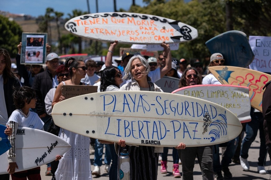 A woman holds a surfboard reading "Beaches, Security, Liberty, Peace" next to members of the surfing community protesting against insecurity after two Australians and an American went missing last week during a surfing trip, in Ensenada, Baja California, Mexico.