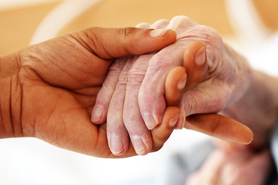 Eine Pflegerin hält die Hand einer Frau - es steht die Warnung vor einem Kollaps der Alten- und Behindertenhilfe im Raum.