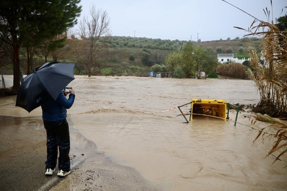 Eine Person fotografiert an einem überlaufenden Flussbett nach dem Durchzug des Sturmtiefs "Leonardo".