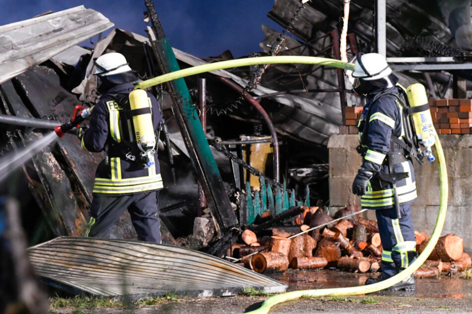 Feuerwehrleute löschen Glutreste in der eingestürzten Lagerhalle.