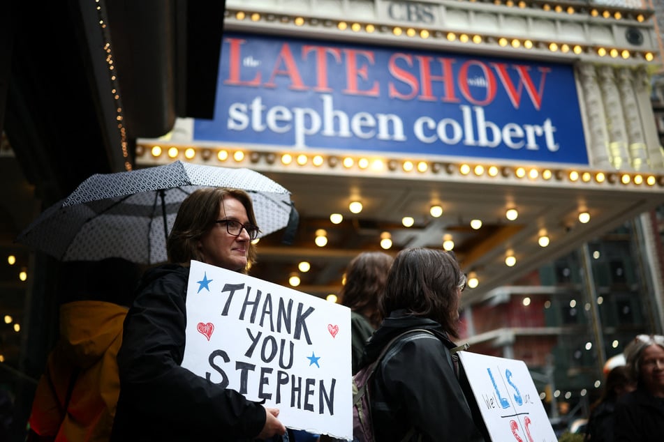 People hold signs supporting Stephen Colbert outside the Ed Sullivan Theater ahead of the taping of the final episode of The Late Show after 32 years on air, in New York on May 21, 2026.