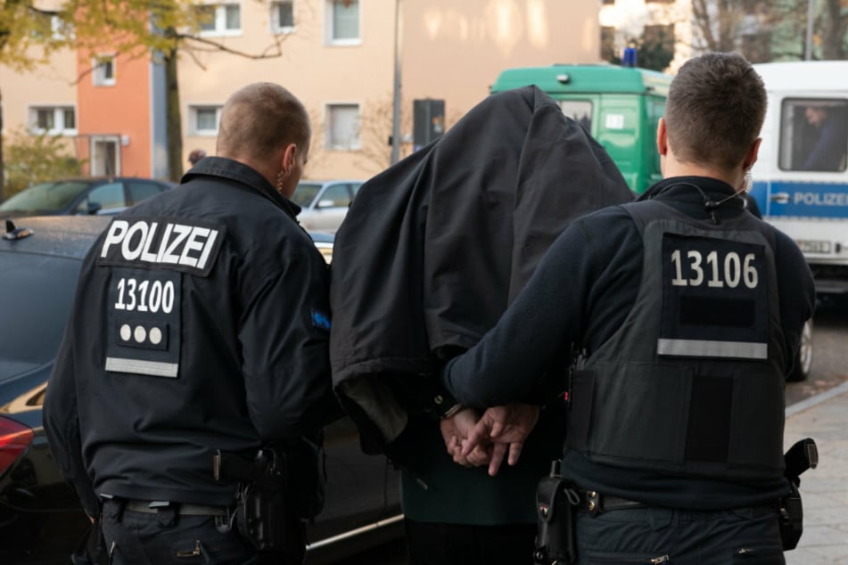 Polizeibeamte führen mit Handschellen einen festgenommenen Mann ab. (Archivbild, Symbolbild)
