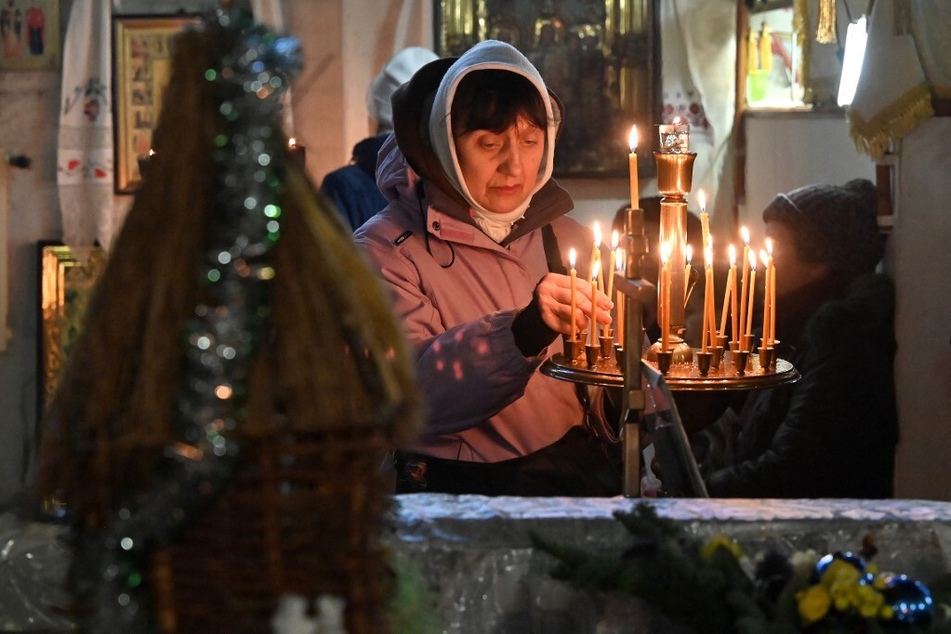 A woman lights a candle during an Orthodox Christmas service mass at the Saint John the Theologian Church in Kharkiv, Ukraine, on December 24, 2023.