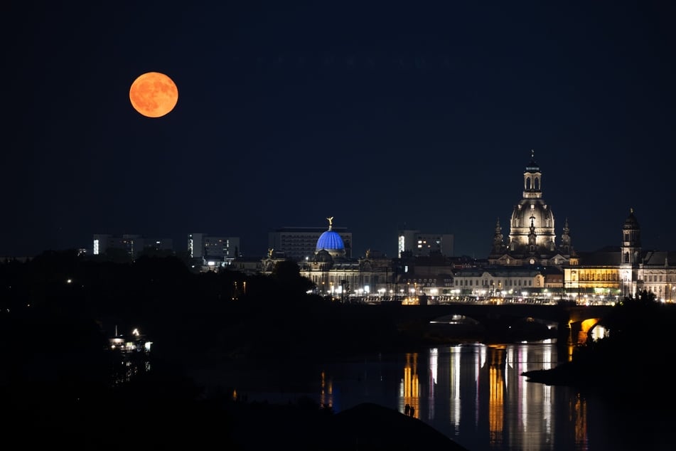 Passanten beobachten am Ufer der Elbe vor der Kulisse der Altstadt den Aufgang des Himmelsspektakels.