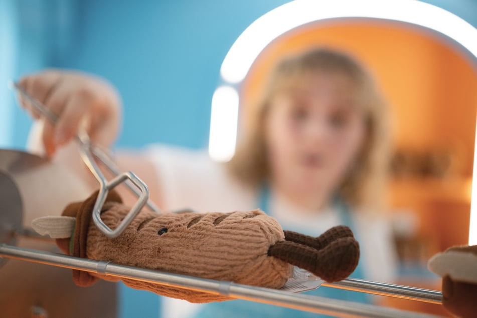 Eine Mitarbeiterin steht während der Eröffnung einer In-Store-Experience der Plüschtiermarke Jellycat im KaDeWe hinter einem Drehspieß mit Plüsch-Bratwürsten.