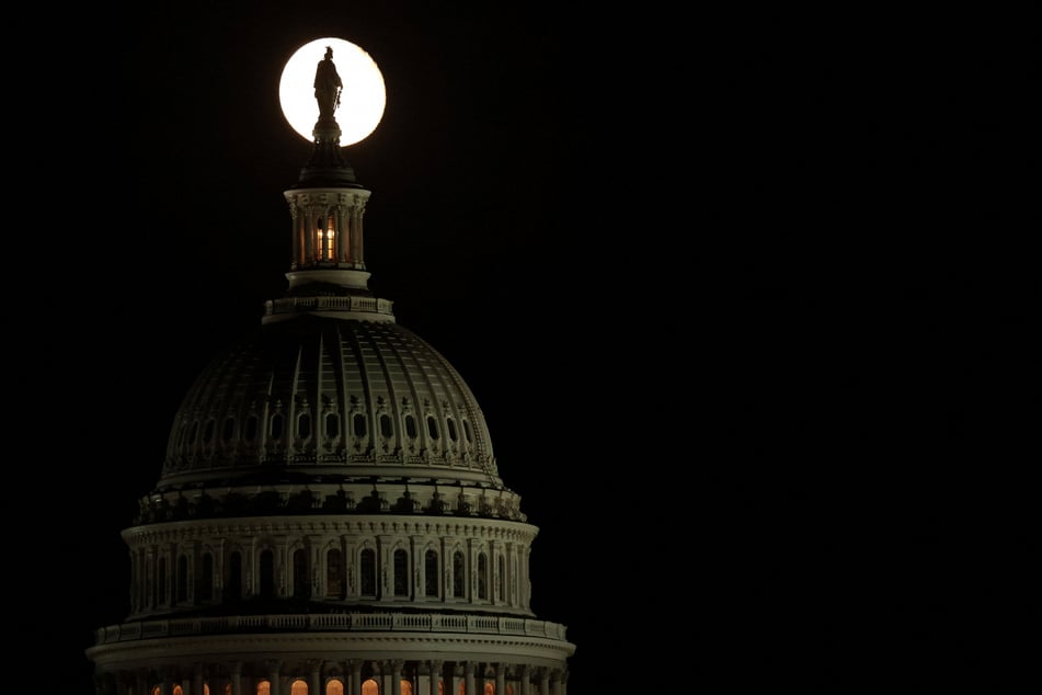 The moon creates a silhouette of the Statue of Freedom atop the US Capitol during a continuing partial federal government shutdown on October 8, 2025.